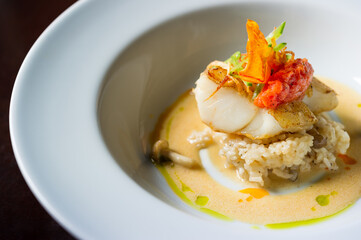 sautéed cod fish with mushroom risotto with broth in a white bowl