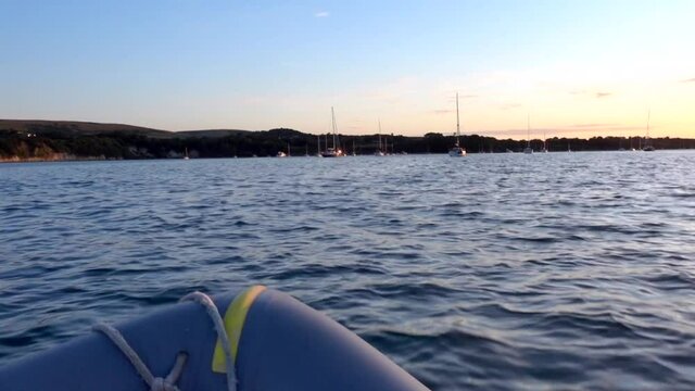 Onboard an inflatable dinghy tender on way across a bay to a yacht as the sun sets.