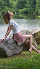 Woman in White Top and Pink Skirt Seated on Large Rock Outside