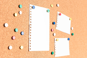 Perspective view of blank papers on a cork board with multi colored thumb tacks around