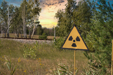 Yellow warning sign indicating radiation in the chernobyl exclusion zone, dangerous red forest in the background. Late afternoon beautiful golden sunset time