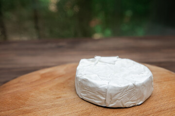 Fototapeta na wymiar a circle of soft brie cheese with white mold from cow's milk on a wooden board on a green bokeh background. place for text