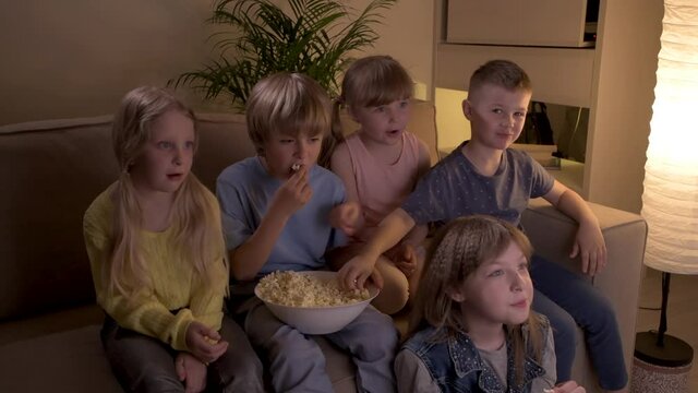 Five lovely children watch cartoon on TV at night, rejoice, laugh and have fun.