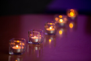 Small lit tea light candles in glass containers in a row on a table top
