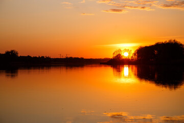 Sunset on the lake, the sun sets behind the trees and beautiful reflections in the water