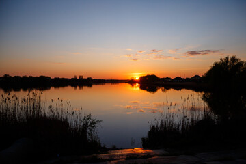 Sunset on the lake, the sun sets behind the trees and beautiful reflections in the water