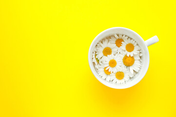 Cup of tea with chamomile flowers on a yellow background. Copy space, top view