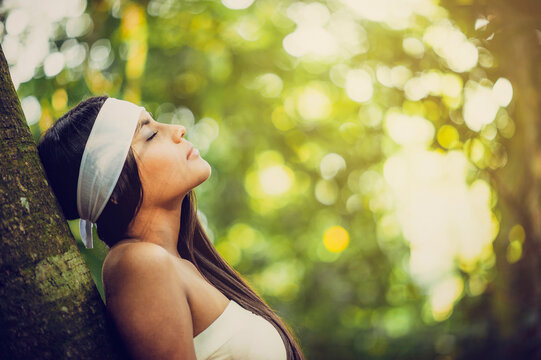 Beautiful woman of indigenous descent relaxing with her eyes closed against a tree