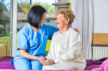 Asian nurse assisting elderly woman on the hospital bed