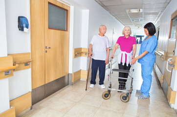 Asian nurse assisting elderly woman with walker walking on the hospital floor