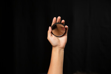 Hispanic woman looking at the mirror with black background - hand holding a small mirror with the reflection of a face in it - hand focused