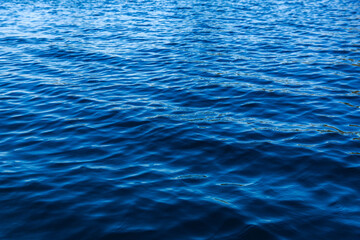 Blue water texture. Waves in a lake background. Sunshine over water and small waves. 