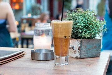 A greek cold coffee, freddo cappuccino placed on a wooden table outdoors, urban background.