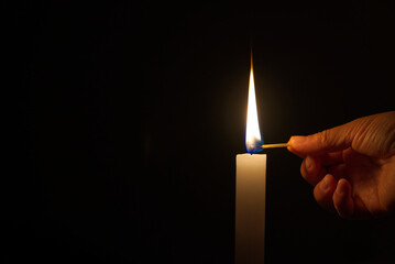 Woman's hand lighting white candle and closeup of burning, black background, copy space