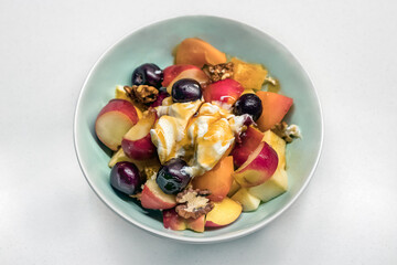 Top view of a home made greek fruit salad with nuts, apple, peach, grapes and yogurt with honey on the top.