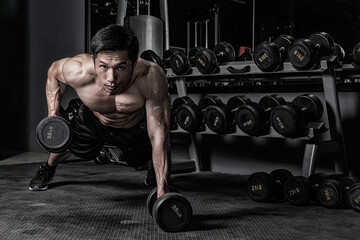 Strong fitness man doing arm workout with dumbbells in the gym