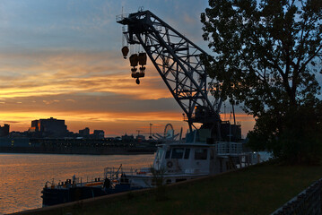 A loader on a boat Montreal with a background of a skyline of river and a city at the time between sunset and twilight. Reflections of sun rays on the river, Saint Laurent river, Montreal.