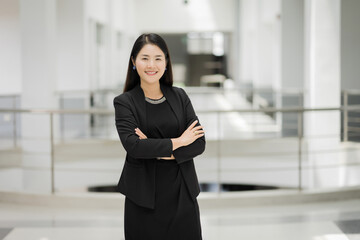 Portrait of a cheerful middle-age businesswoman in business suit stands in the company building with confidence arms crossed. Modern business woman in the office with copy space. Business stock photo.