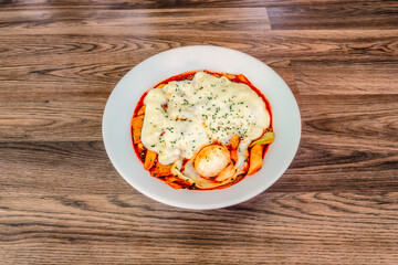 Korean Cheese Tteokbokki at a 45 degree angle on a wood table in a white bowl.