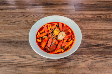Korean Budae Tteokbokki at a 45 degree angle on a wood table in a white bowl.
