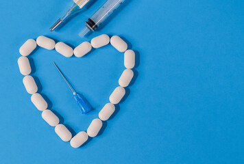 White heart made of pills and a disposable syringe with a needle on the left and a place for text...