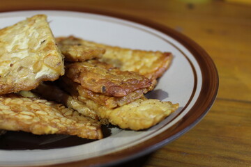 Fried tempeh for snack on plate. Made by a natural culturing and controlled fermentation process that binds soybeands into a cake form. selective focus