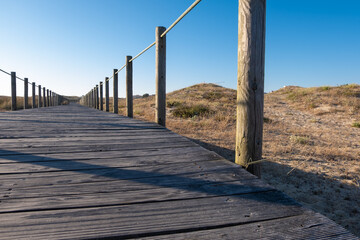 Fototapeta premium Wooden walkway over sand dunes at beach in Portugal on a summer day. Low angle.