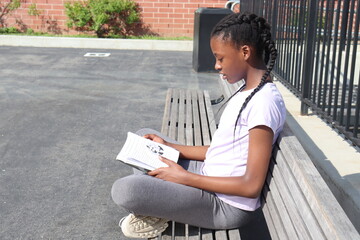 Black Girl sitting on a park bench reading a book