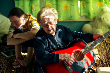 An elderly old woman plays guitar for her granddaughter.