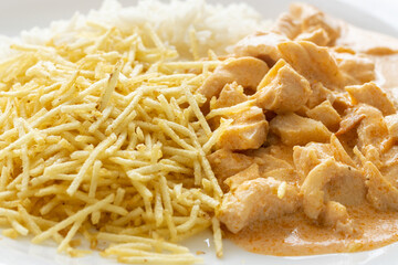 Strogonoff servido em prato branco com batata palha e arroz branco. Comida gostosa.