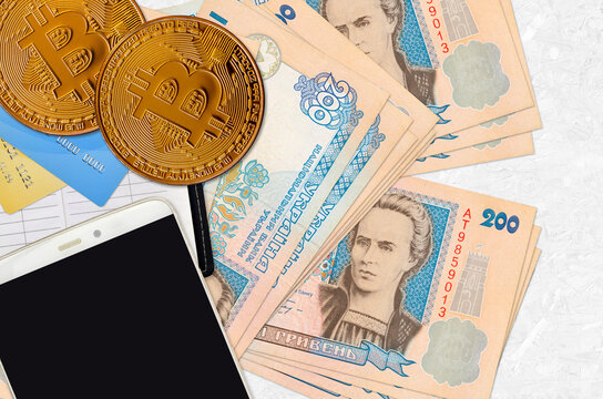 200 Ukrainian hryvnias bills and golden bitcoins with smartphone and credit cards. Cryptocurrency investment concept. Crypto mining or trading