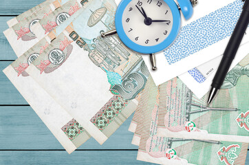 20 Thai Baht bills and alarm clock with pen and envelopes. Tax season concept, payment deadline for credit or loan. Financial operations using postal service