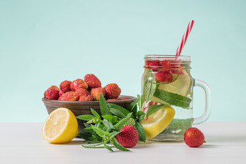 A refreshing drink of berries, lemon and mint and a bowl of strawberries on a white table.