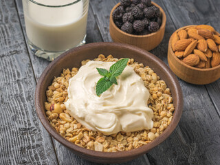 A bowl of granola, yogurt, and mint leaves on a wooden table. 