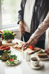 Close up photo of a caucasian couple preparing breakfast together in the kitchen slicing bread and vegetables