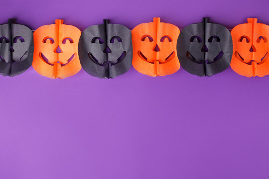 Halloween paper garland with black orange pumpkin jack-o-lantern hanging on the purple wall. Easy crafts for kids. Copy space for your text, October holiday banner, festive party idea