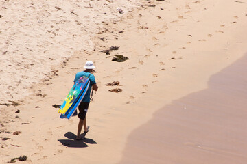 Man Walking Along Beach With Body-Boards over Shoulder