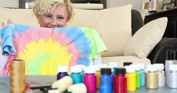 Pleased woman holding and showing her own painted tie dye tshirt concept of female hobby and leisure time activity