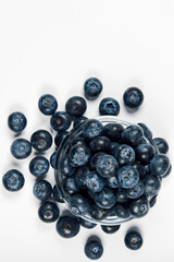 Freshly juicy picked blueberries in glass bowl isolated on white background. Top view. Selective focus. Free text space. Concept of healthy eating and nutrition..