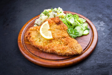 Traditionelles frittiertes Wiener Schnitzel mit Kartoffel und Gurken Salat angeboten as close-up auf einem rustikalen Holz Schneidebrett