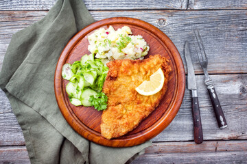 Traditional deep-fried schnitzel with potato and cucumber salad offered as top view on a rustic wooden board with copy space