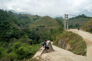 Fototapeta premium Woman sits looking at a bridge in Mường Hoa Valley near Sapa in Vietnam