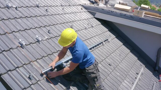 Young Caucasian man on steep roof attaching and installing install solar panel hardware on sunny day, close up static