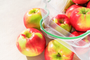 Fresh ripe and juicy apples in reusable eco-friendly mesh bag lie on the table. Sunny day. Plastic free, zero waste and sustainable lifestyle concept. Reusable using. Closeup view.
