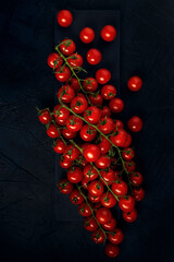 A trusses bunch of red wet cherry tomatoes on serving board and dark textured background. Vegetable composition. Flat lay. Space for text.