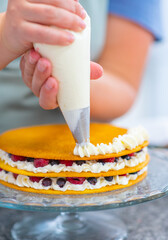 Pastry chef hands squeeze cream from a pastry bag onto a cake