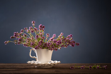 thyme flowers in white vintage cup on wooden table on blue background