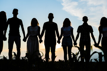 Cohesion concept. A group of friends are holding hands at sunset.