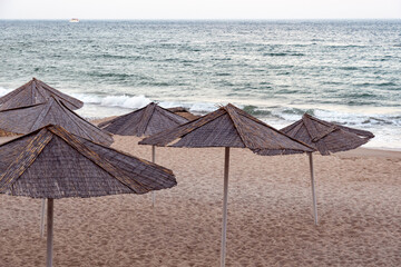 beach umbrellas on beach sand. Palm rattan parasols on beach near ocean surf