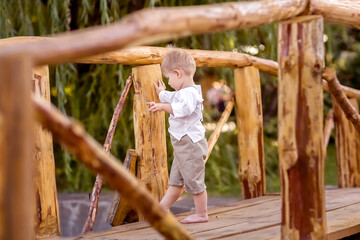 A little boy stands on a bridge over the river. The boy thought about it. The boy is cheerful. Nature walk.